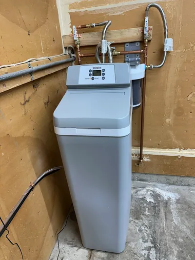 A cabinet-style water softener installed in a garage with bypass and isolation valves